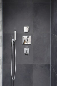 Donker betegelde douchewand met chromen armaturen
