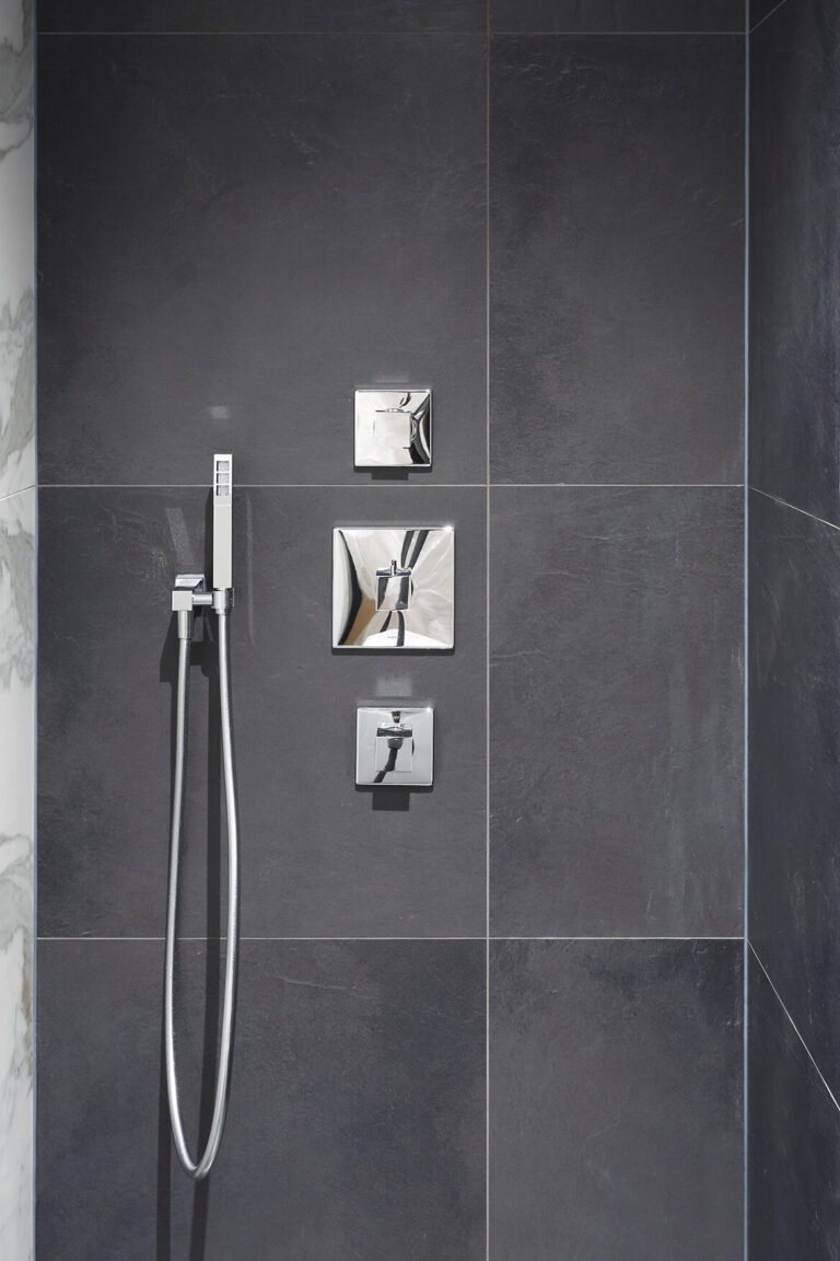 Donker betegelde douchewand met chromen armaturen